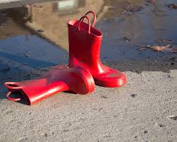 Red rain boots sitting on pavement with a puddle behind them.