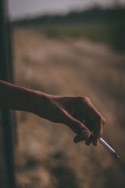 A left hand holding a cigarette against a soft tan background.