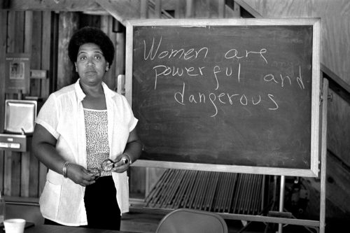 Audre Lorde posing with a chalkboard that reads women are powerful and dangerous